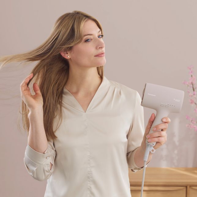 Panasonic EH-NA0L-P825 Panasonic EH-NA0L vysoušeč vlasů nanoe MOISTURE+ Mineral (1600 W, 4 režimy, tryska pro zvětšení objemu, tryska pro silnější proudění vzduchu), růžový 8 Lifestylový snímek ženy, která si suší vlasy vysoušečem vlasů Panasonic Nanocare EH-NA0L v růžové barvě Sakura Pink.
